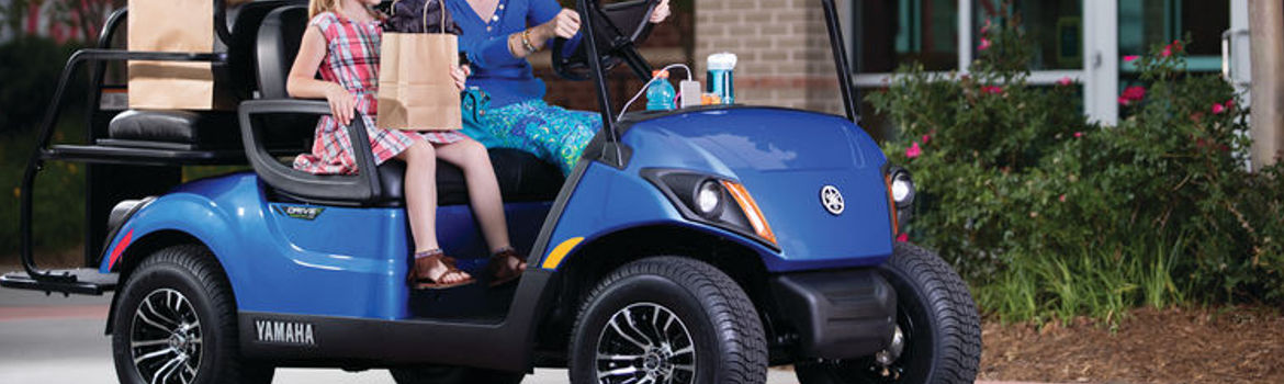 Woman and child riding in a 2018 Yamaha Golf Car past building